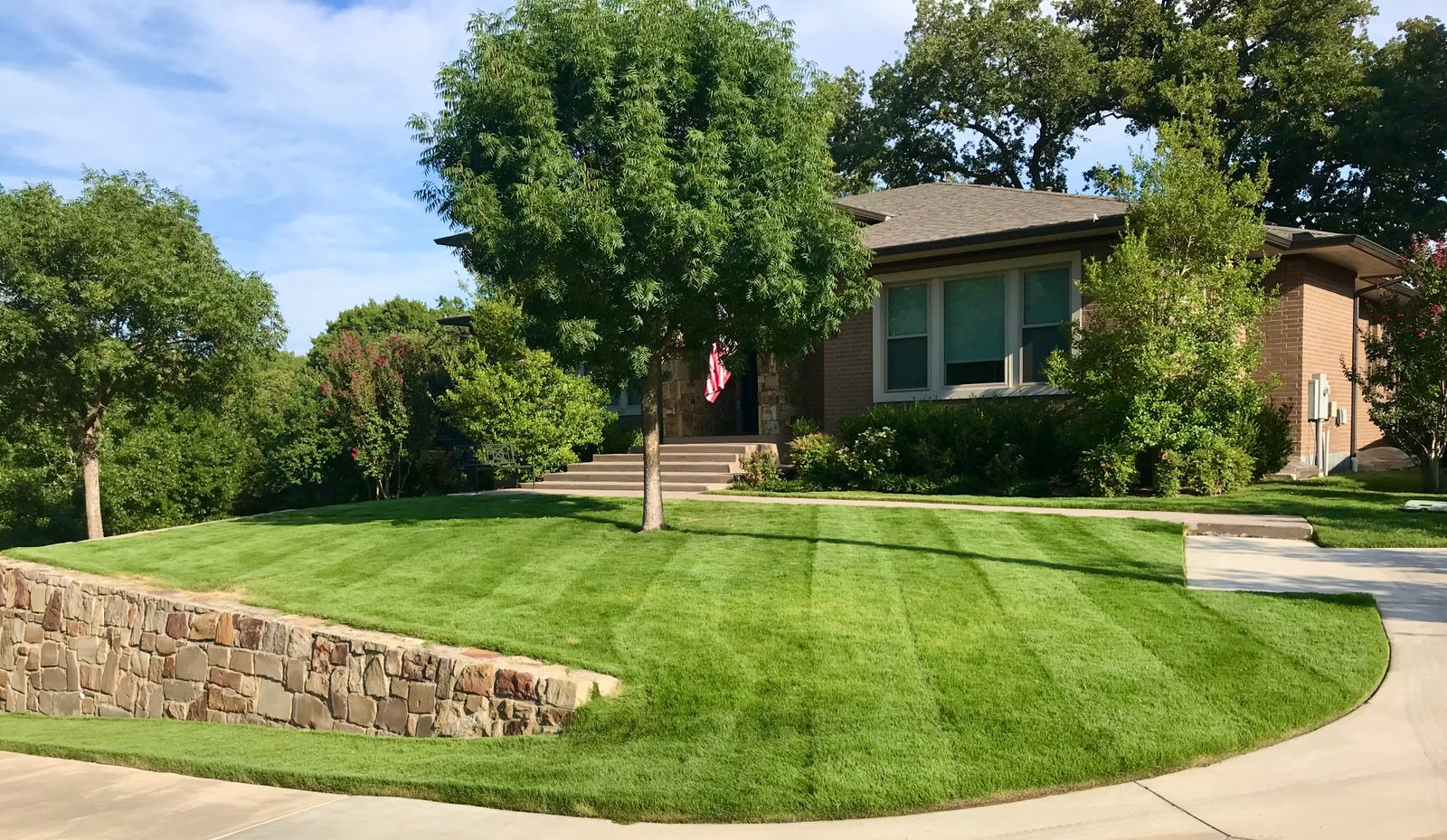 Striped green front lawn curving around a stone retaining wall in front of a brick home in Grapevine, TX