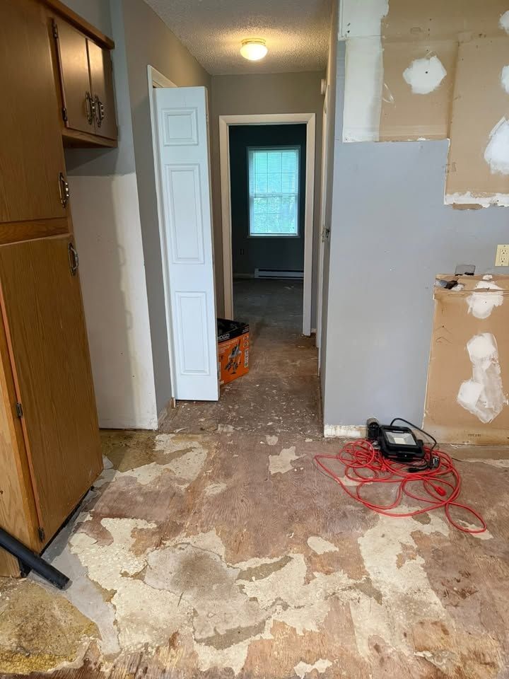 Kitchen partway through demolition, looking down a hallway, with the floor pulled up to the subfloor and a red extension cord on the ground