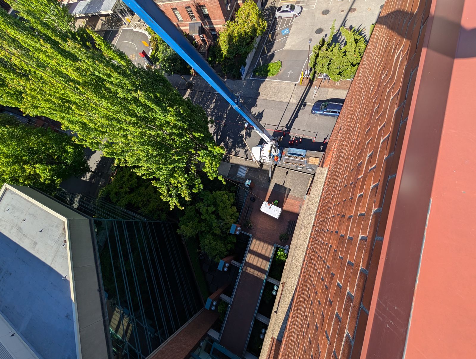 View down the brick face of a commercial building to a blue boom lift and the street below