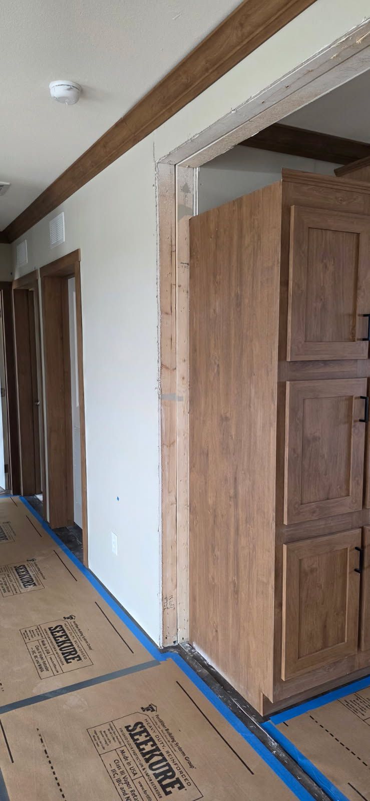 Stained wood door and trim in a hallway with floor protection paper laid down