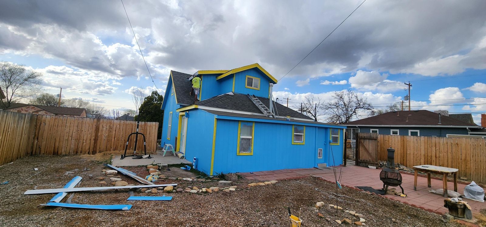 Blue cottage partway through an exterior repaint, with the yard in front