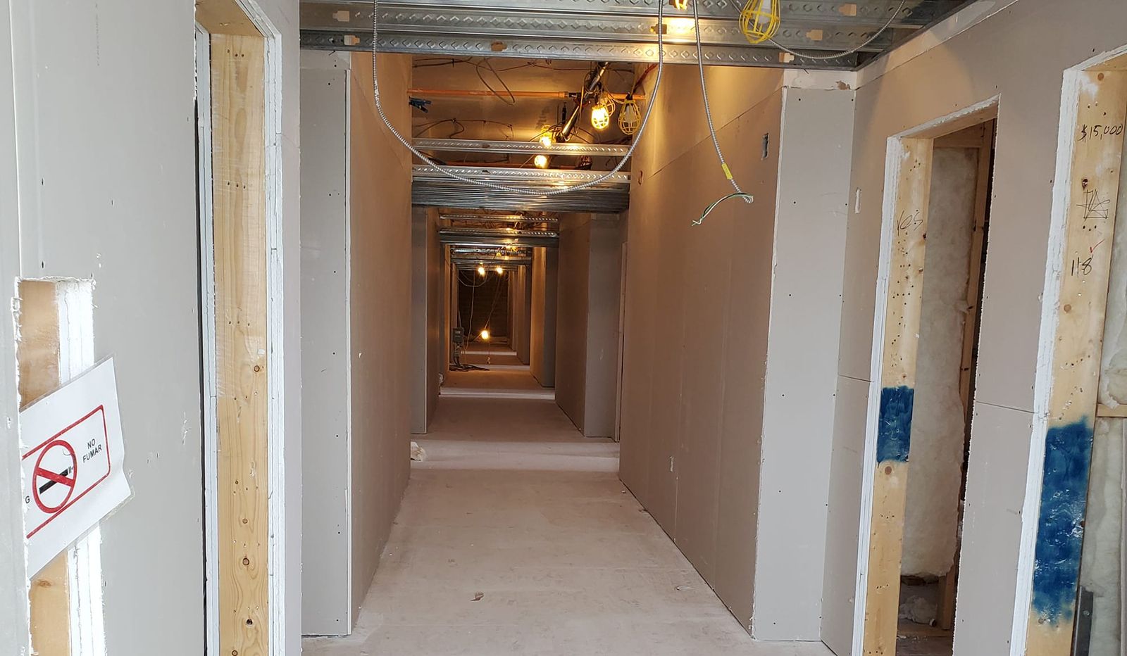 Long corridor with new drywall hung and taped, framing visible, ready for mud coats