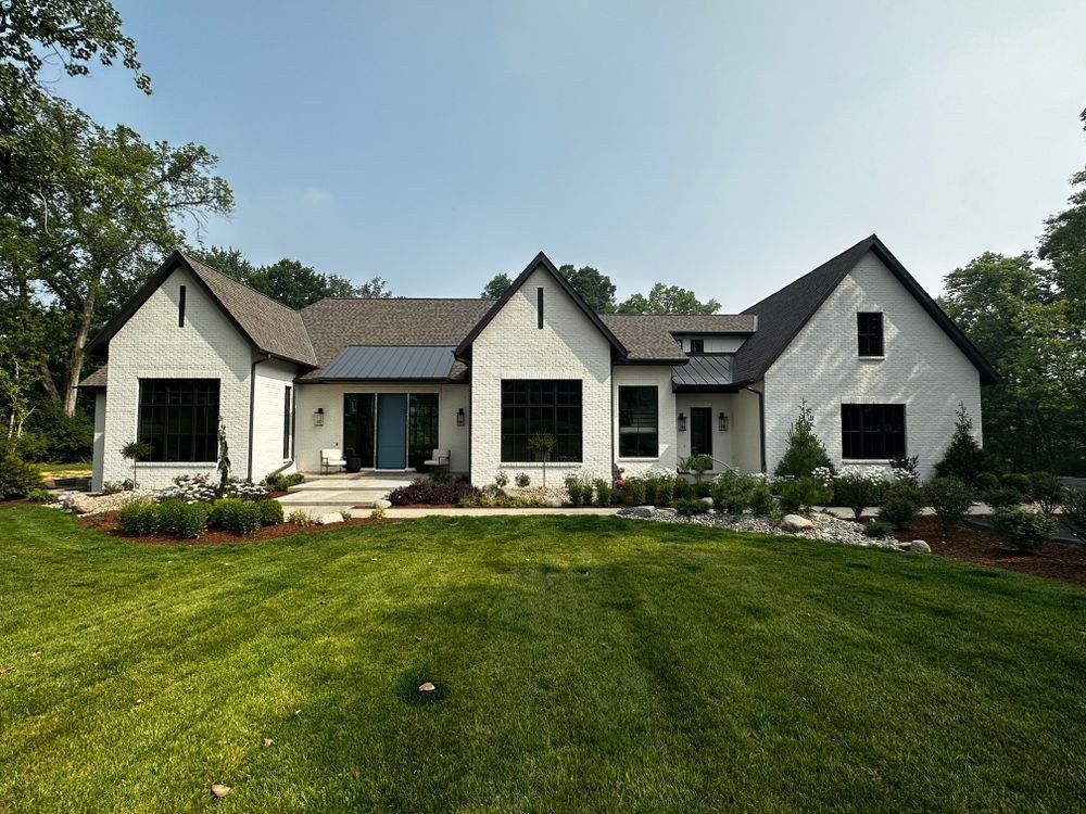White limewashed brick home with black windows and a landscaped lawn