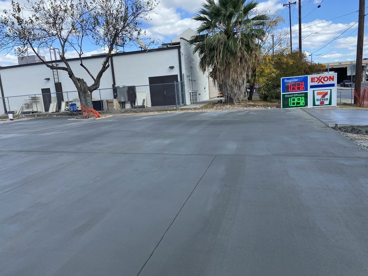 Newly poured concrete parking lot at a commercial gas station property with a palm tree and clear sky
