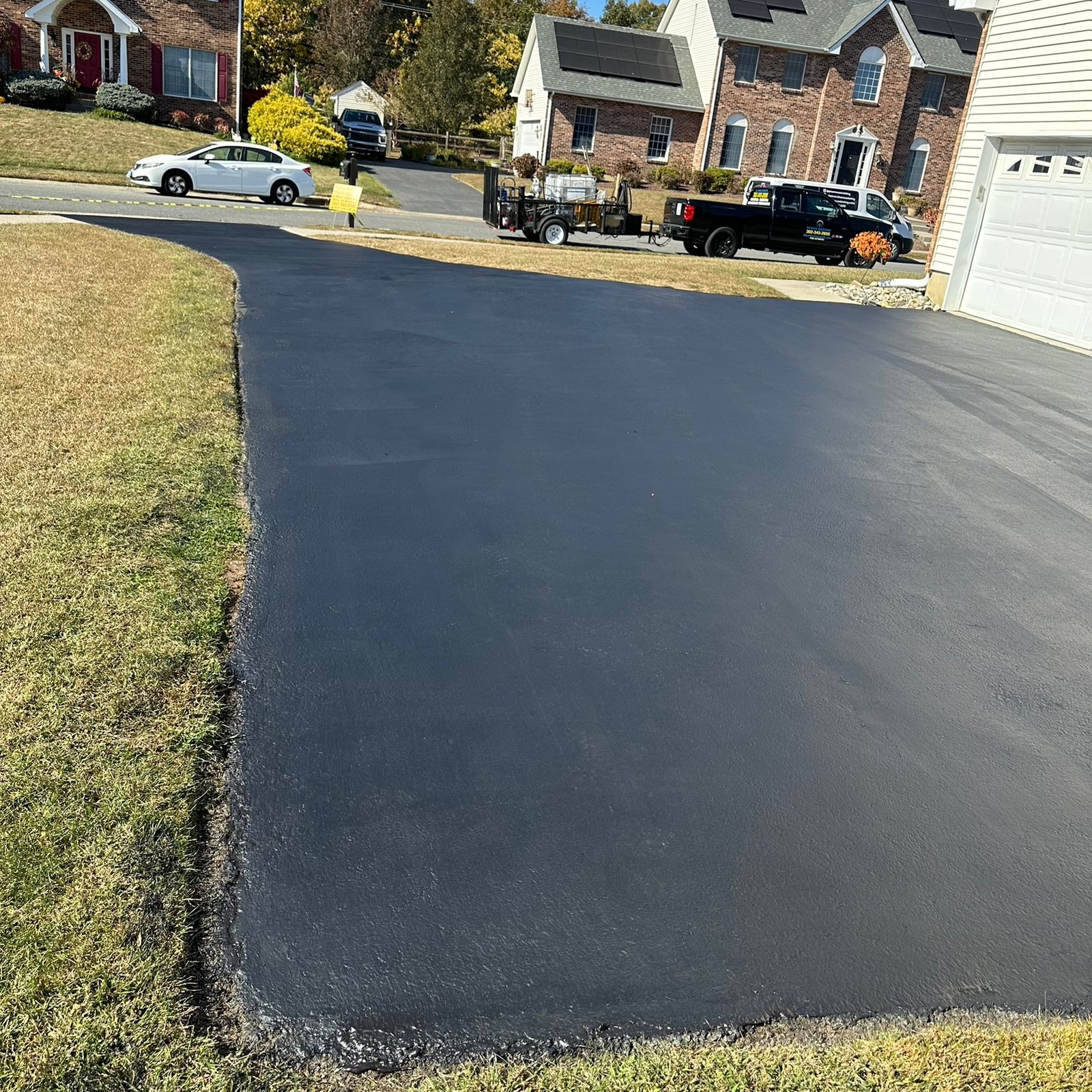 Freshly sealcoated blacktop driveway curving down to the street, with the work truck parked at the kerb
