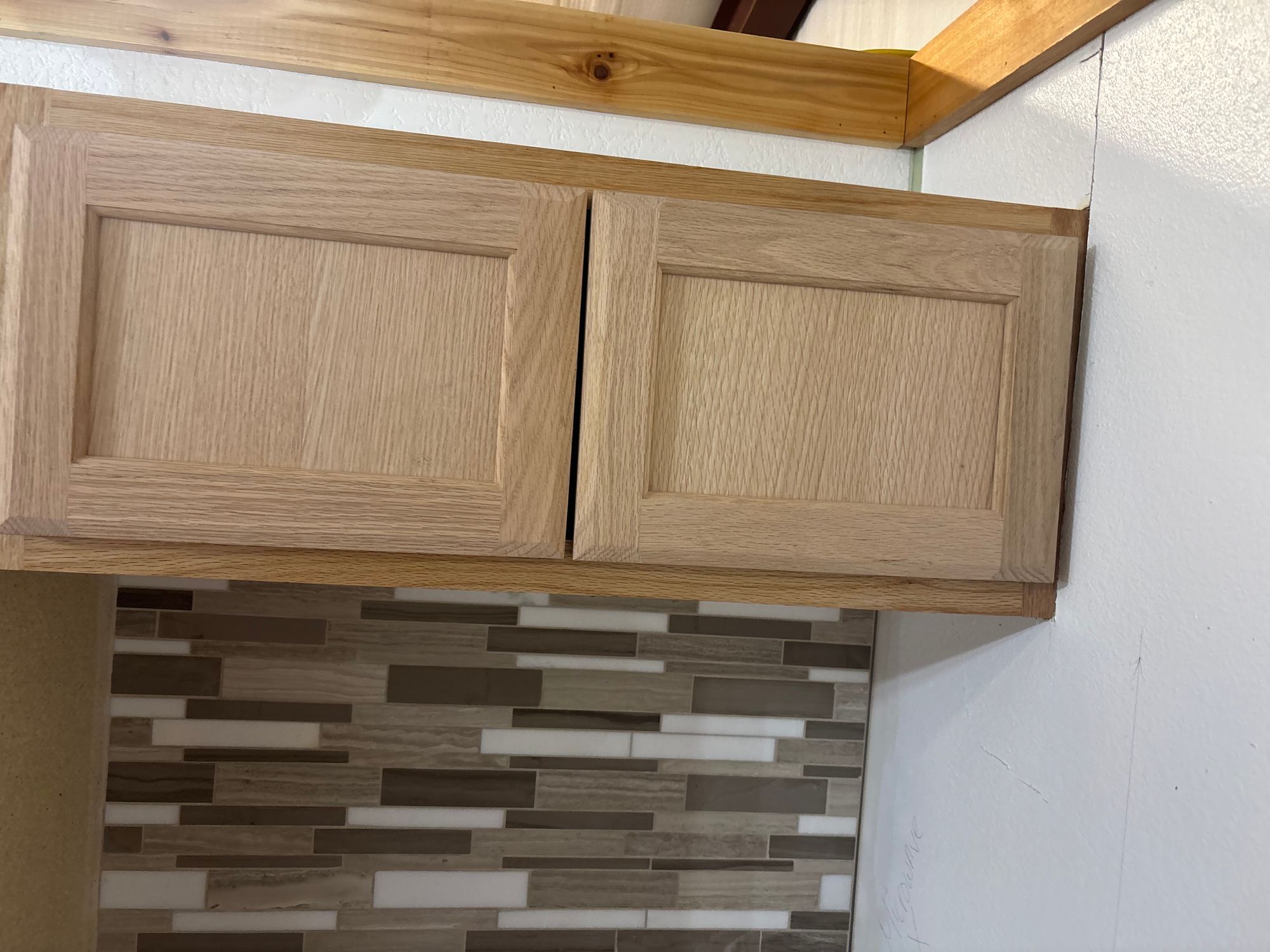Mosaic tile backsplash installed under oak kitchen cabinets