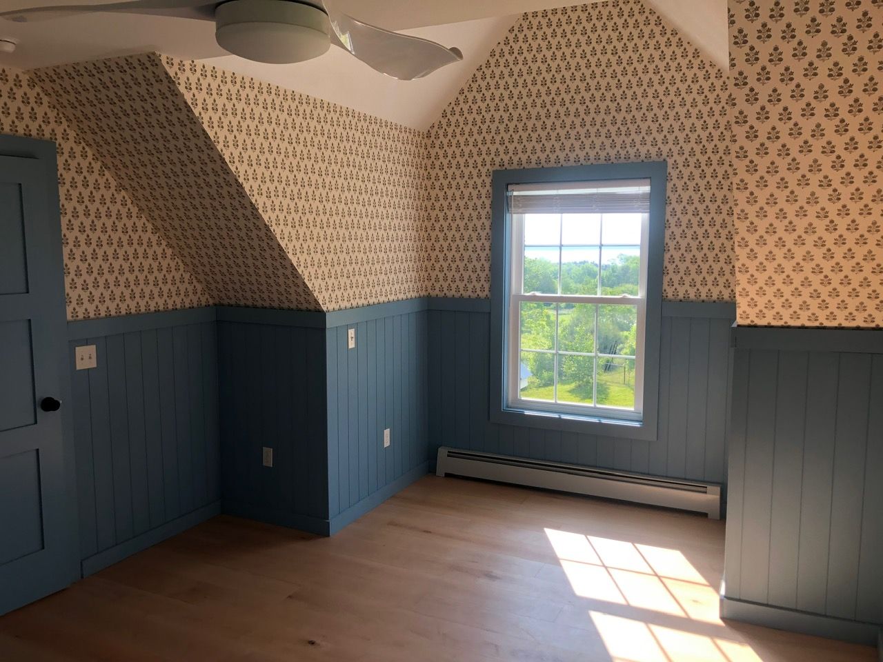 Upstairs bedroom with new wallpaper above blue painted beadboard wainscot