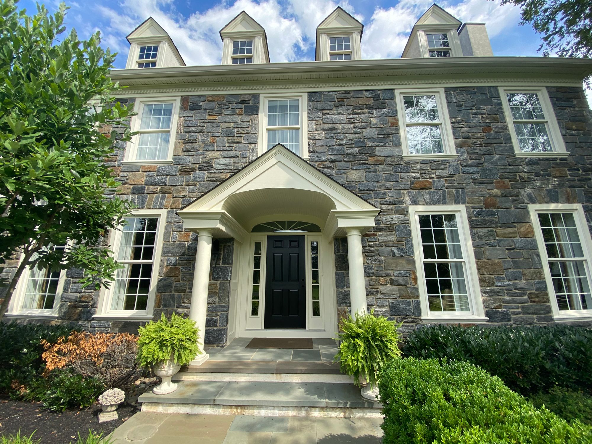 Stone colonial with freshly painted white trim, portico and black shutters