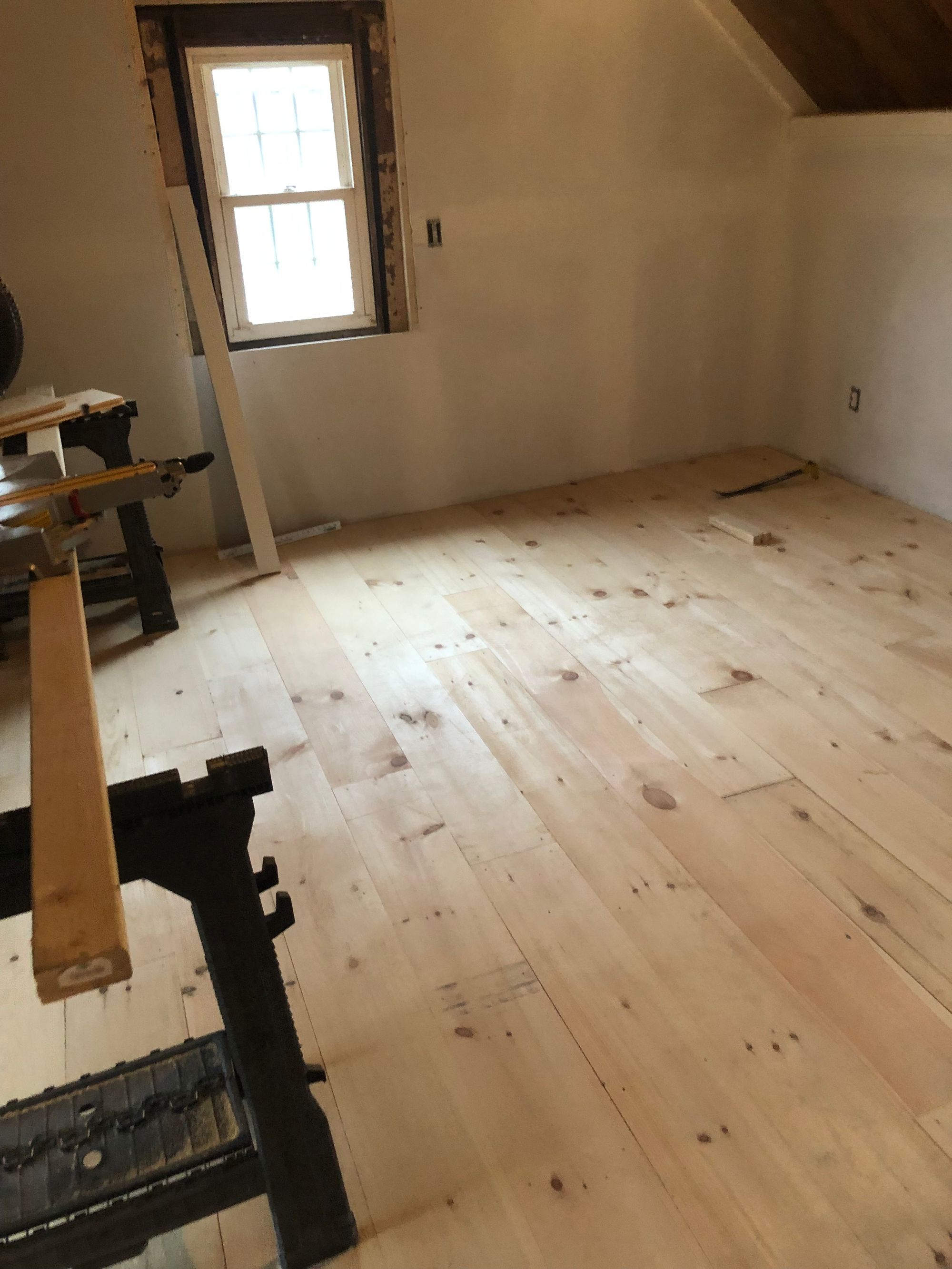 Wide pine floorboards in a finished attic room with a window