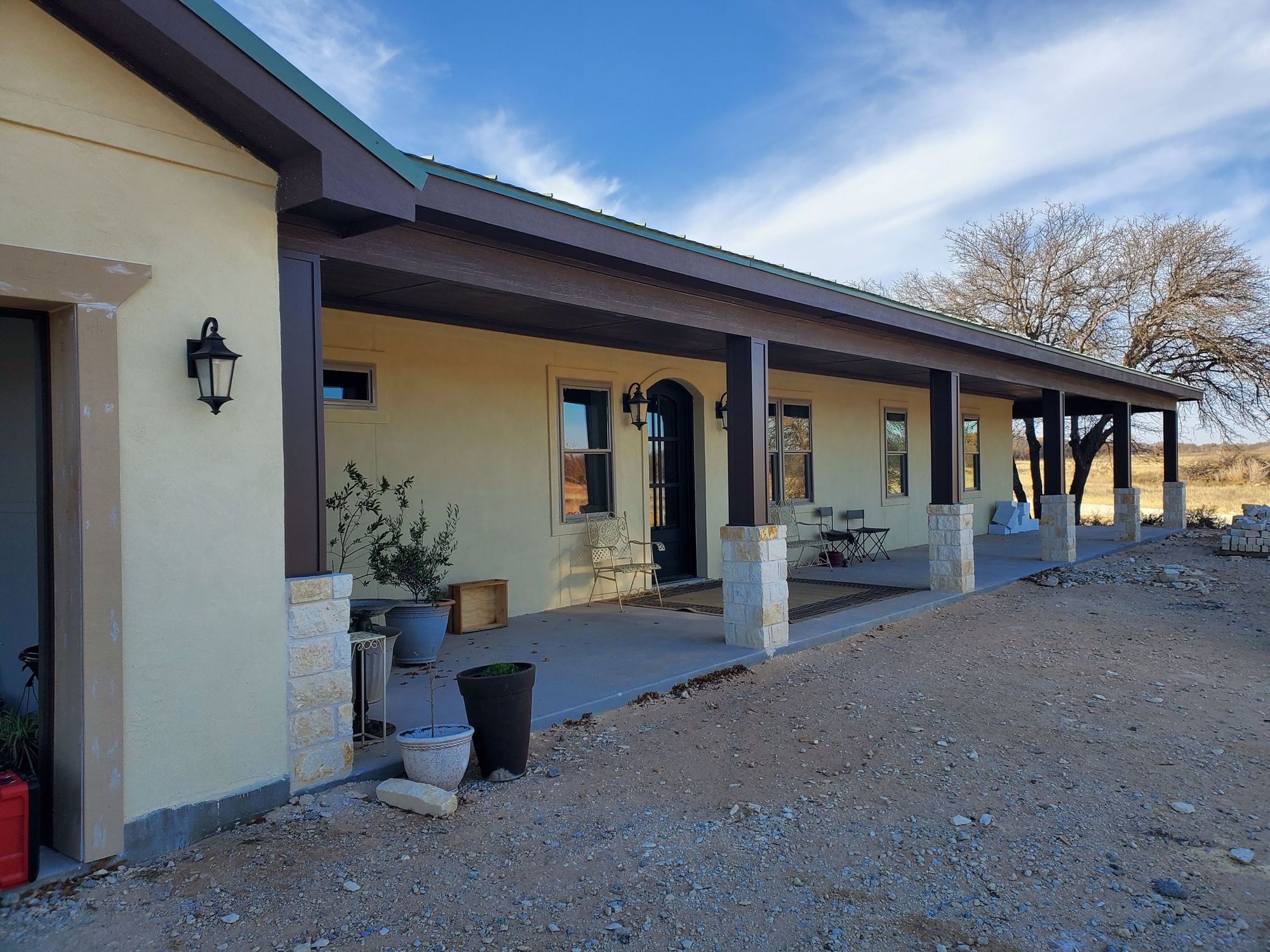 Single-story stucco custom home in Anson, Texas with a long covered porch, stone-based columns and a standing-seam metal roof
