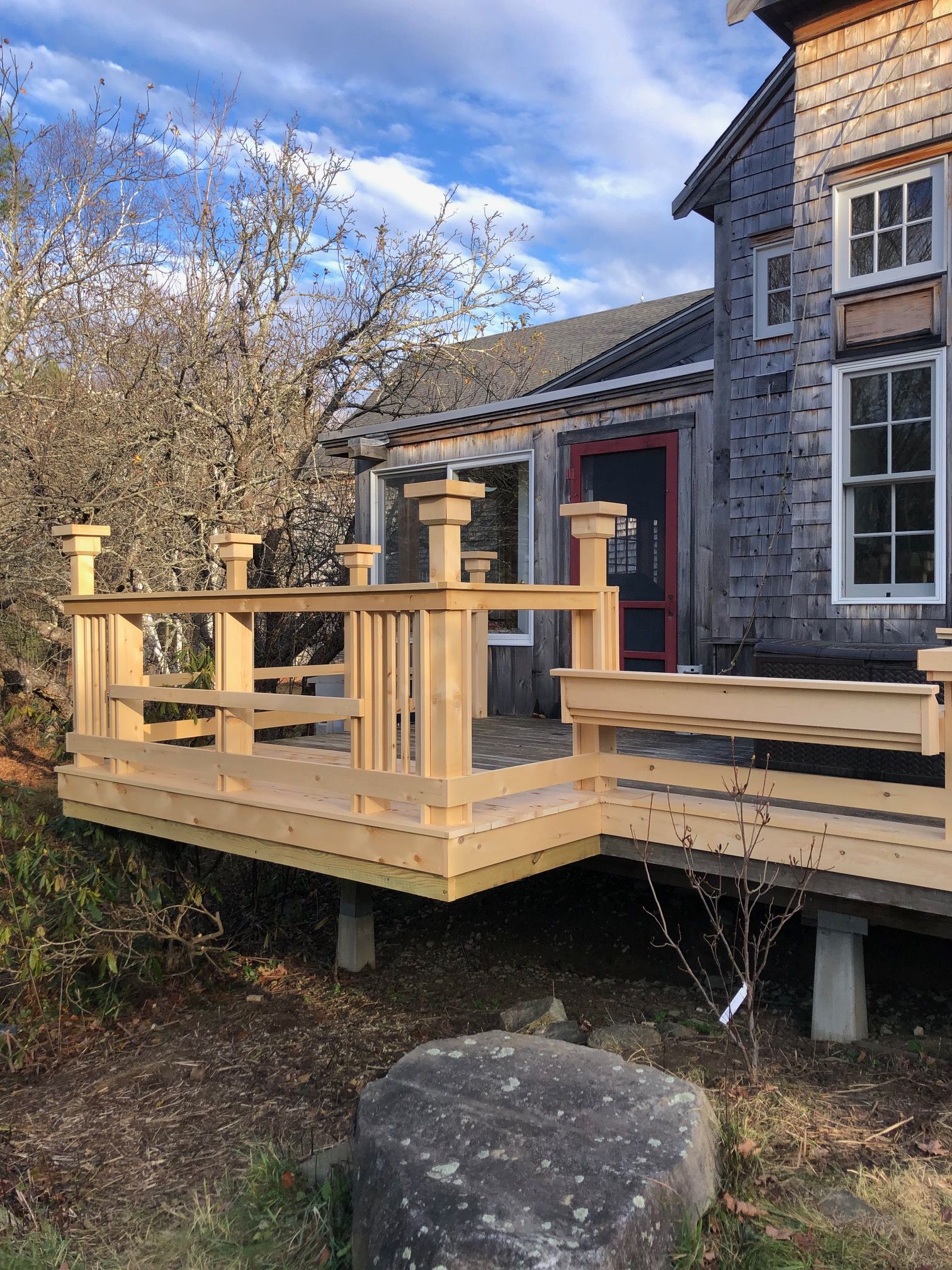 New cedar deck with railings and stepped post caps beside a shingled house