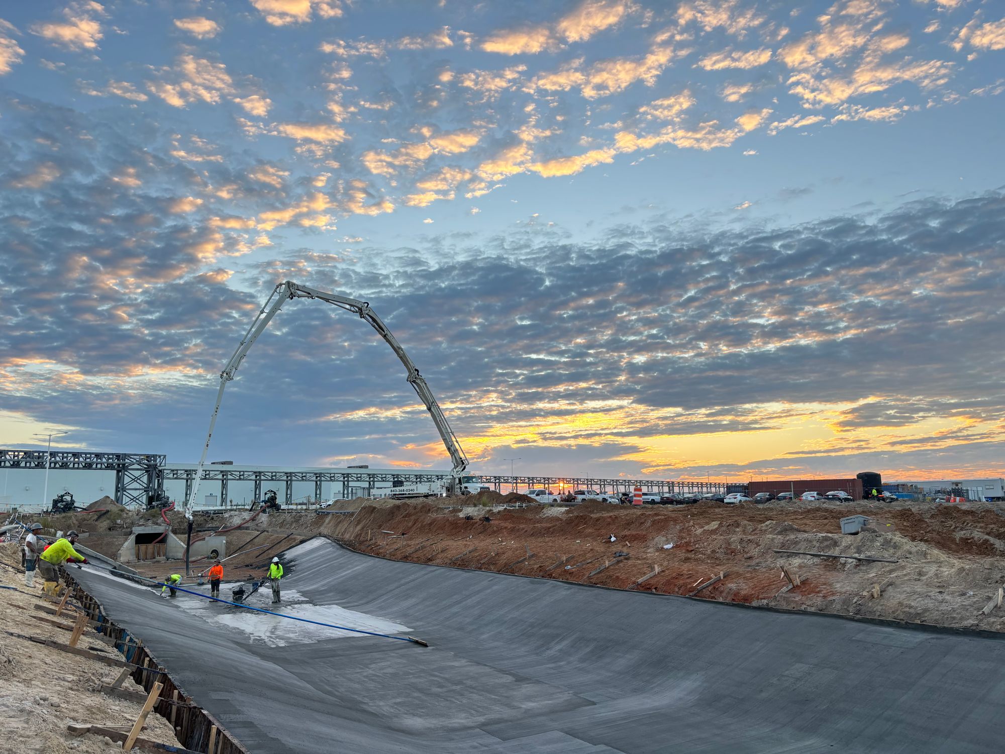 Merced Concrete LLC crew placing a large concrete pour with a boom pump at sunset