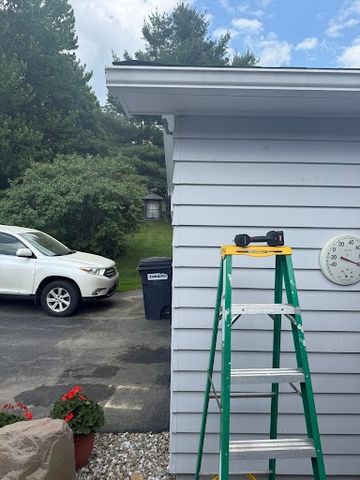 Green stepladder with a cordless drill resting on its top step, leaning against the gray siding of a house
