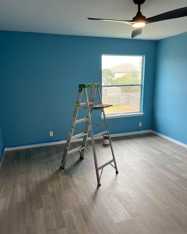 Bedroom repainted in a bright blue with white baseboards and a step ladder still in the room