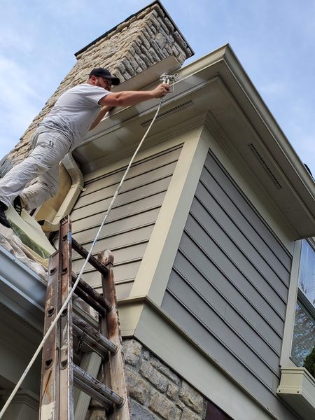 Painter on a ladder brushing the fascia and eaves beside a stone chimney