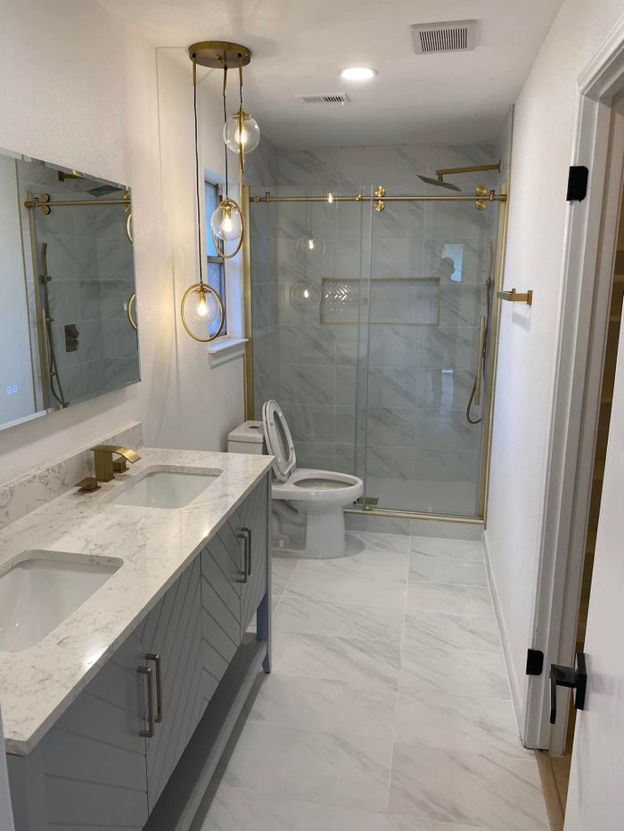 Remodeled bathroom with a glass shower, gold fixtures and a double vanity
