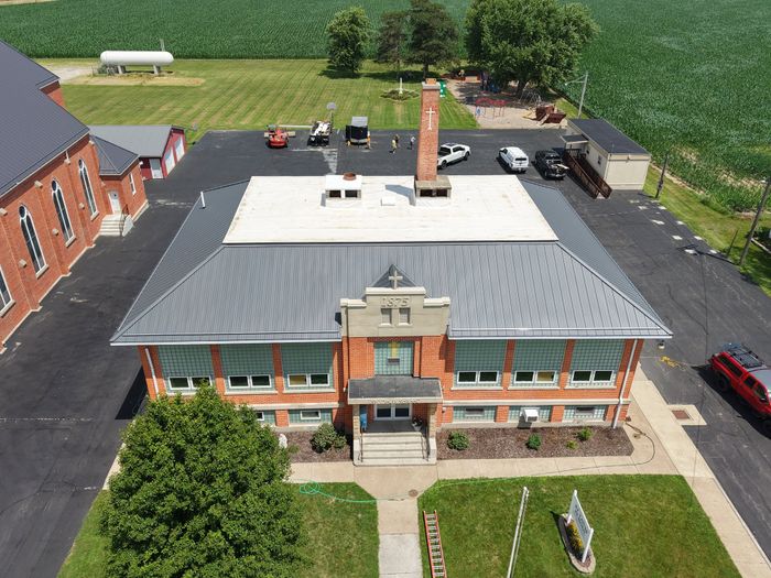 Aerial view of a large brick building topped with a charcoal metal roof