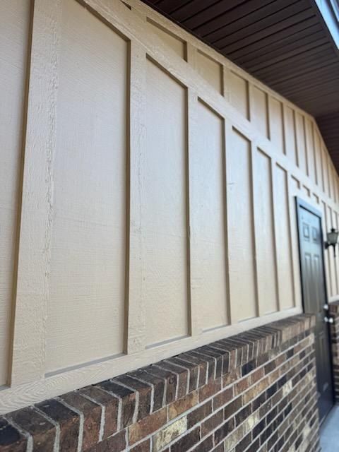 Freshly painted board-and-batten siding in tan above a brick base