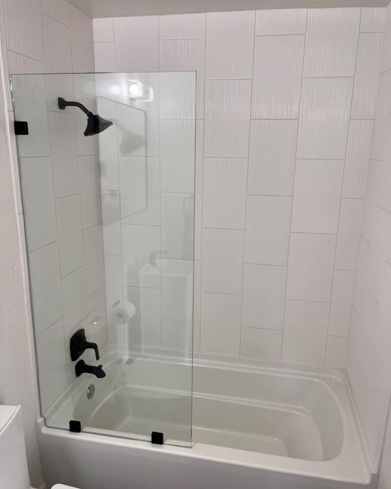 Frameless glass shower panel over a tub with black fixtures
