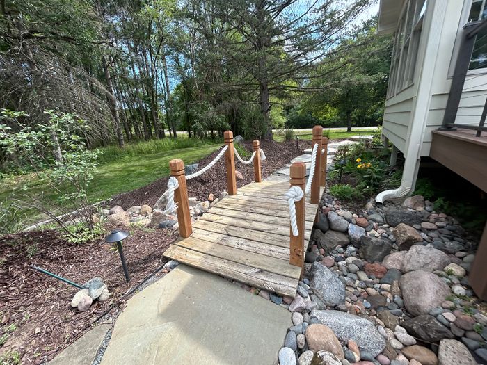 Wooden footbridge with rope railings over a river rock creek bed