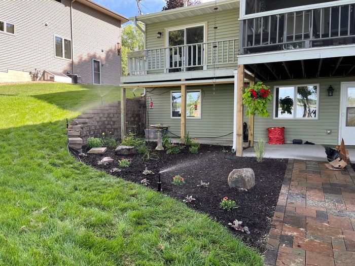 Curved planting bed with boulders and mulch along a lawn and paver walk