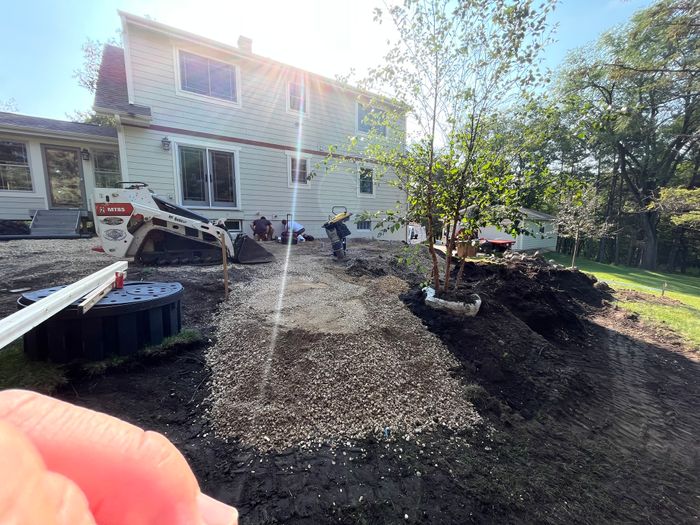 Skid steer spreading gravel base beside a house