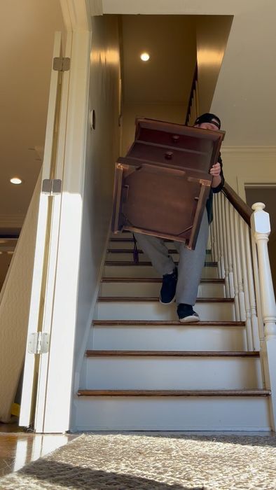 A mover carrying a wooden dresser down a carpeted staircase
