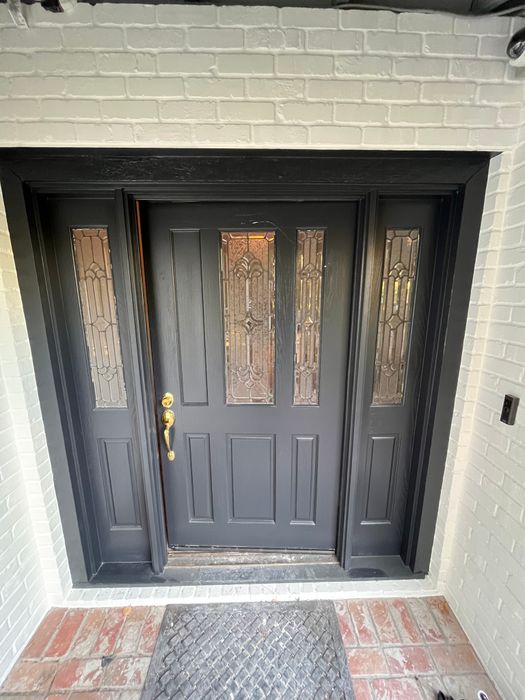 Black front door with decorative glass sidelights and a brick surround