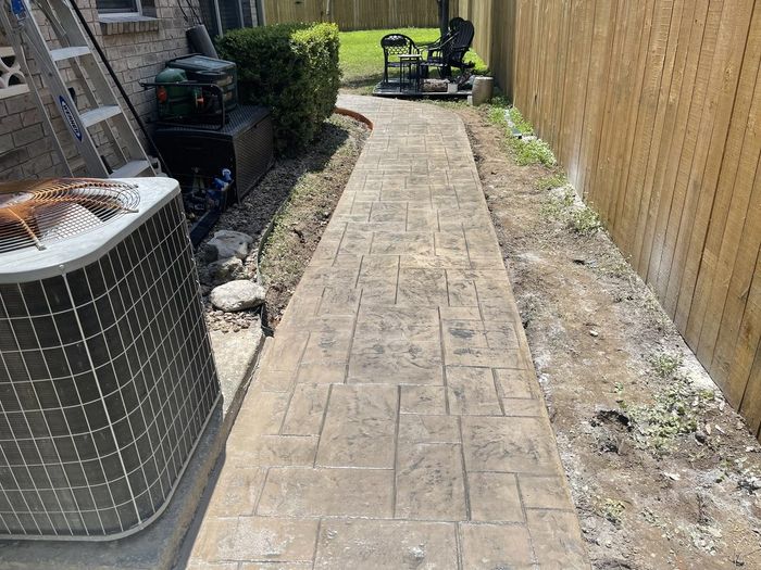 Stamped ashlar-pattern concrete walkway running along a brick home to the backyard