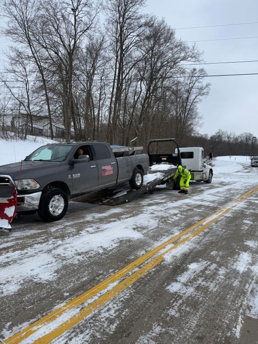 Pickup with a plow mount and a trailer on a snowy road with a person in a safety vest