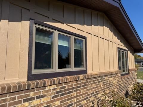Tan siding with dark brown window trim above brick