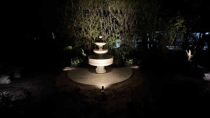 Fountain lit at night in a landscaped yard