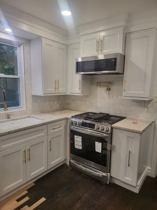 Renovated kitchen with white shaker cabinets, gold hardware and a new range