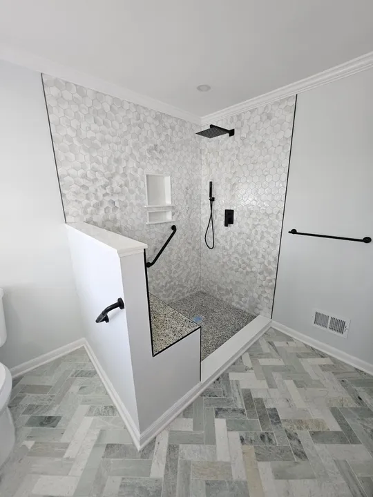 Walk-in shower with herringbone tile floor and matte black fixtures