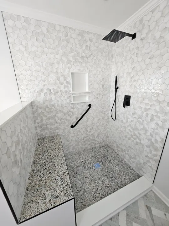 Walk-in shower tiled in white hexagon tile with a pebble floor and bench