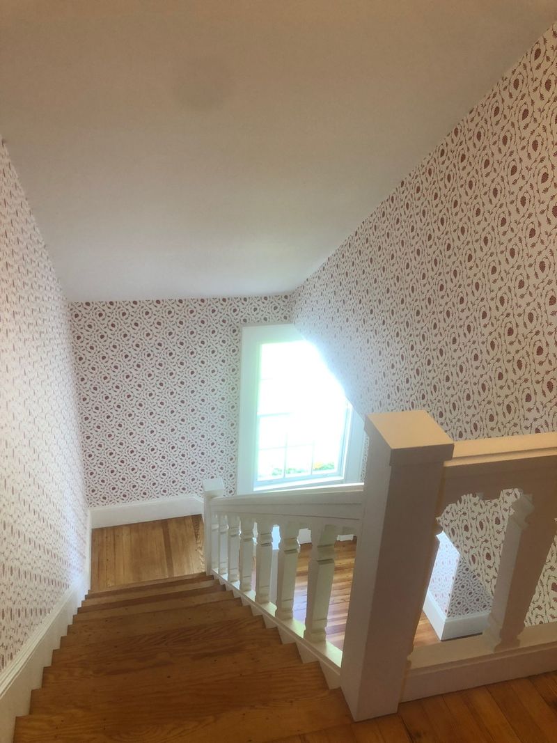 Stairwell papered in a red pattern beside a white stair rail