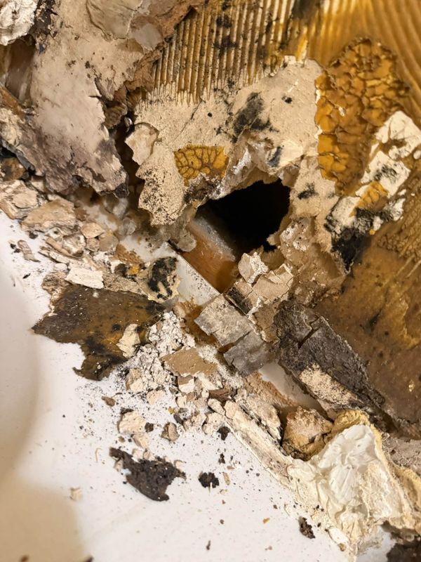 A hole in the wall at the edge of a bathtub, with broken, darkened board around it