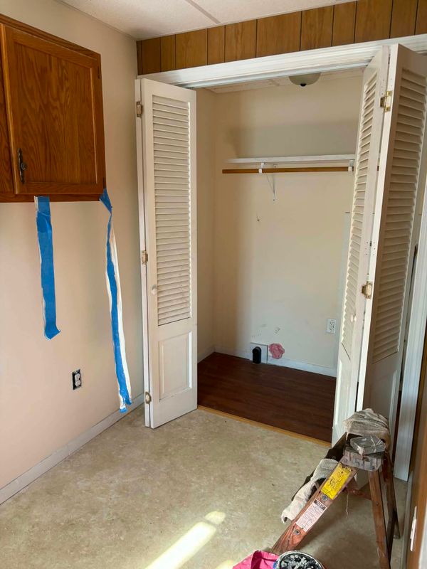 Closet with louvered doors and blue tape along the walls, ready for painting