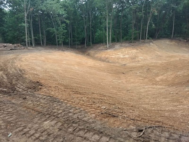 Smooth shaped pond basin with sloped sides and track marks, with woods behind