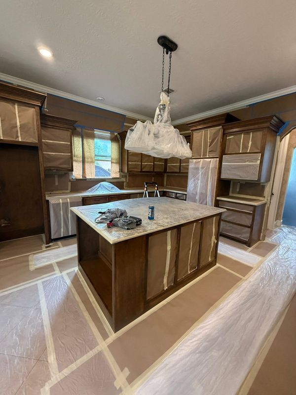 Kitchen with cabinets and an island, with the floor and counters masked in paper and tape