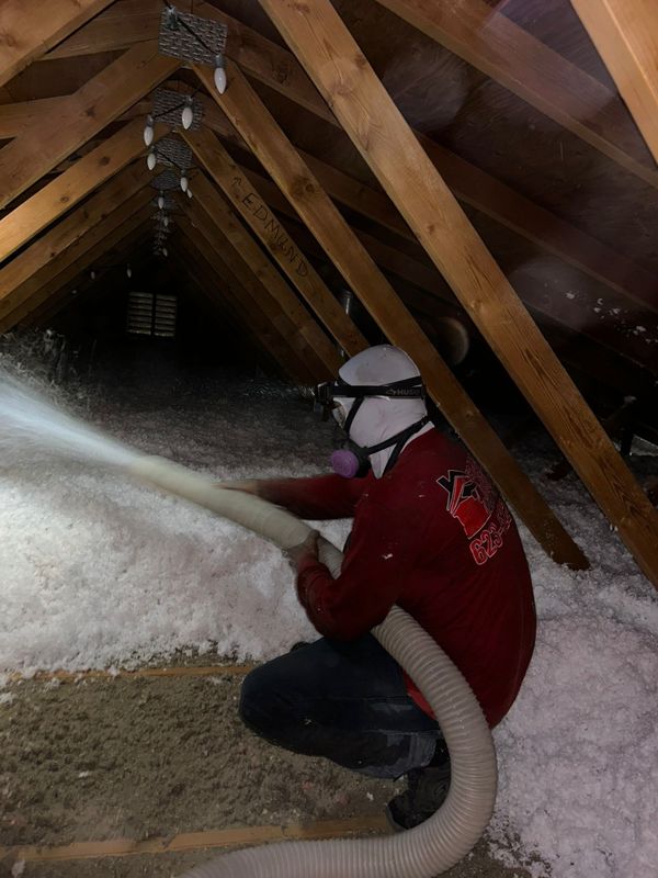 Foam Pro technician in a respirator spreading blown-in fiberglass between attic joists