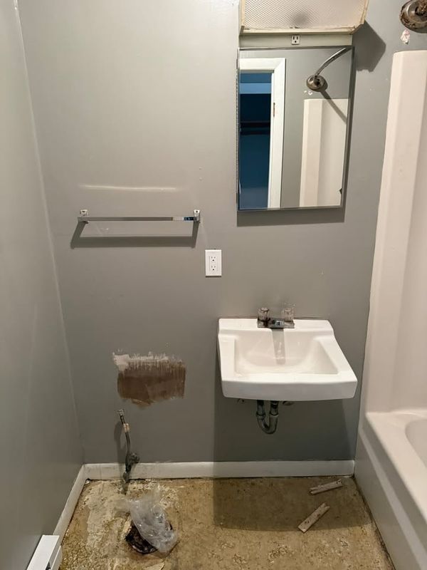 Bathroom wall cut open beside a wall hung sink, with scraps of debris on the floor