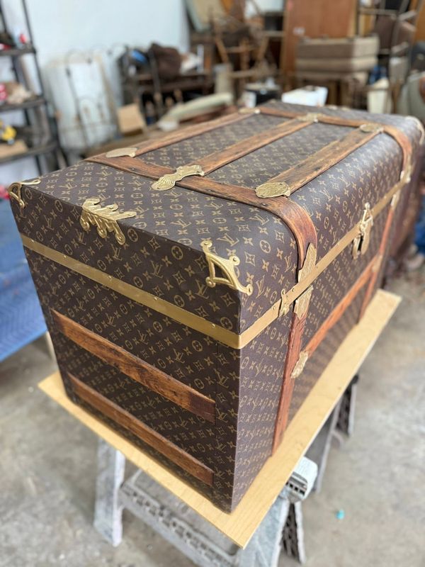 Antique steamer trunk covered in monogram-pattern canvas with brass corners and wood slats