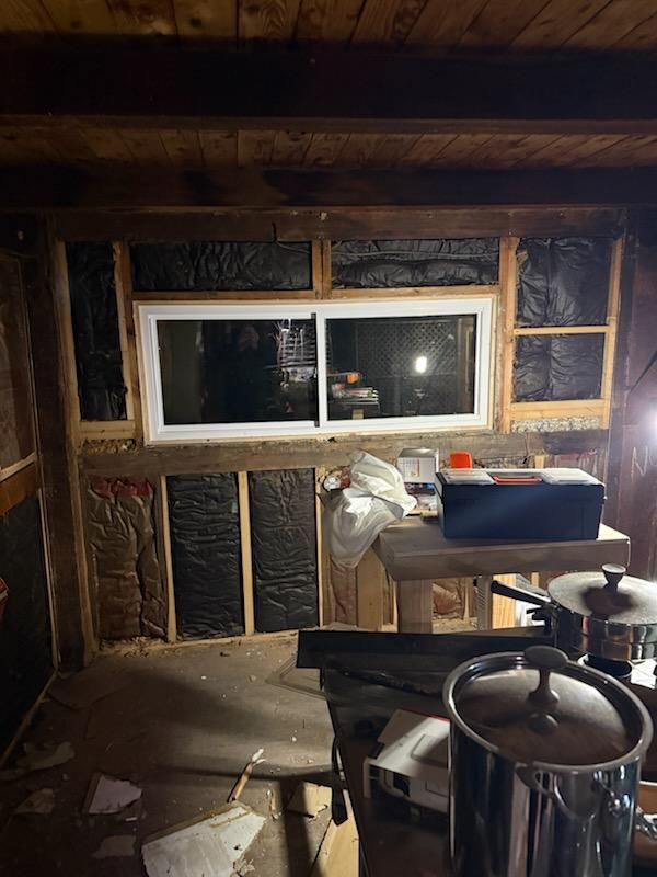 Insulation packed between the studs around a new window, with a toolbox and work bench in the room