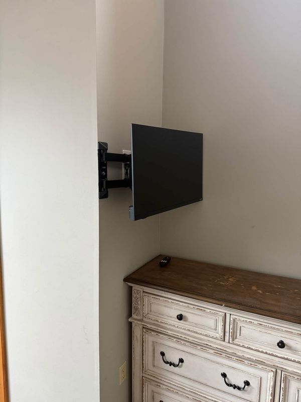 Flat screen television on a swing arm bracket, turned out from the wall in a corner above a dresser