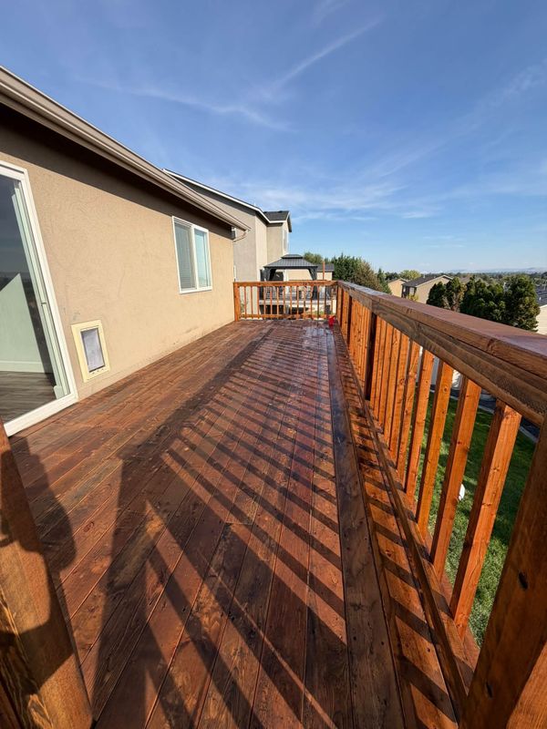 Long stained deck with a railing in morning light on a stucco home