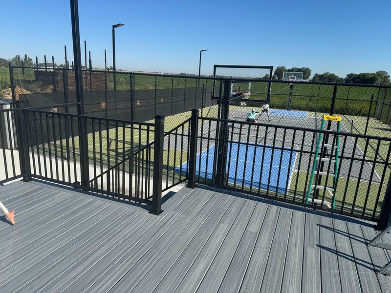 Composite deck with black aluminum railing over a sport court and farm field