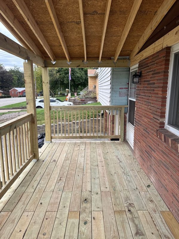 New wood-framed covered porch with decking and railings beside a brick wall
