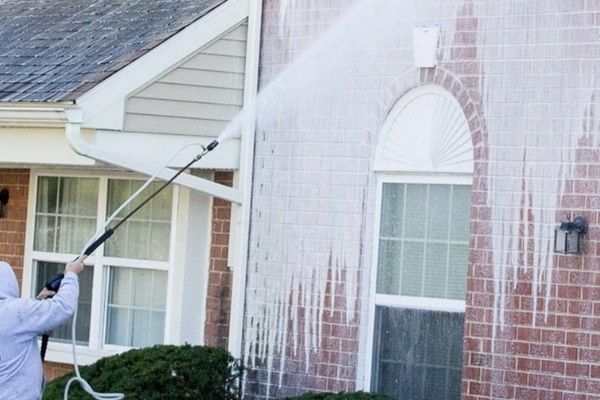 Soft washing a brick house exterior with low-pressure spray and cleaning solution