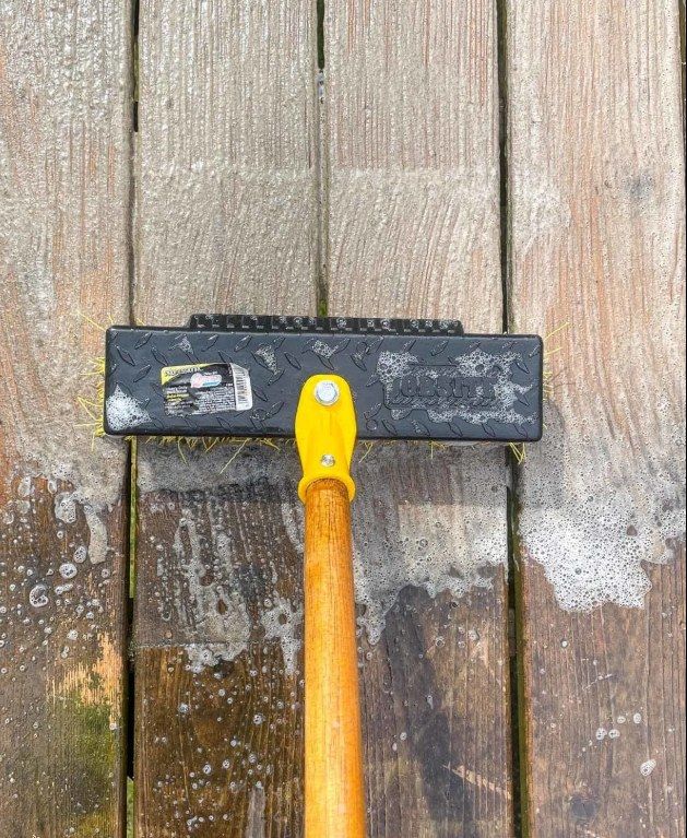 Scrub brush and soap suds on a weathered wooden deck during cleaning